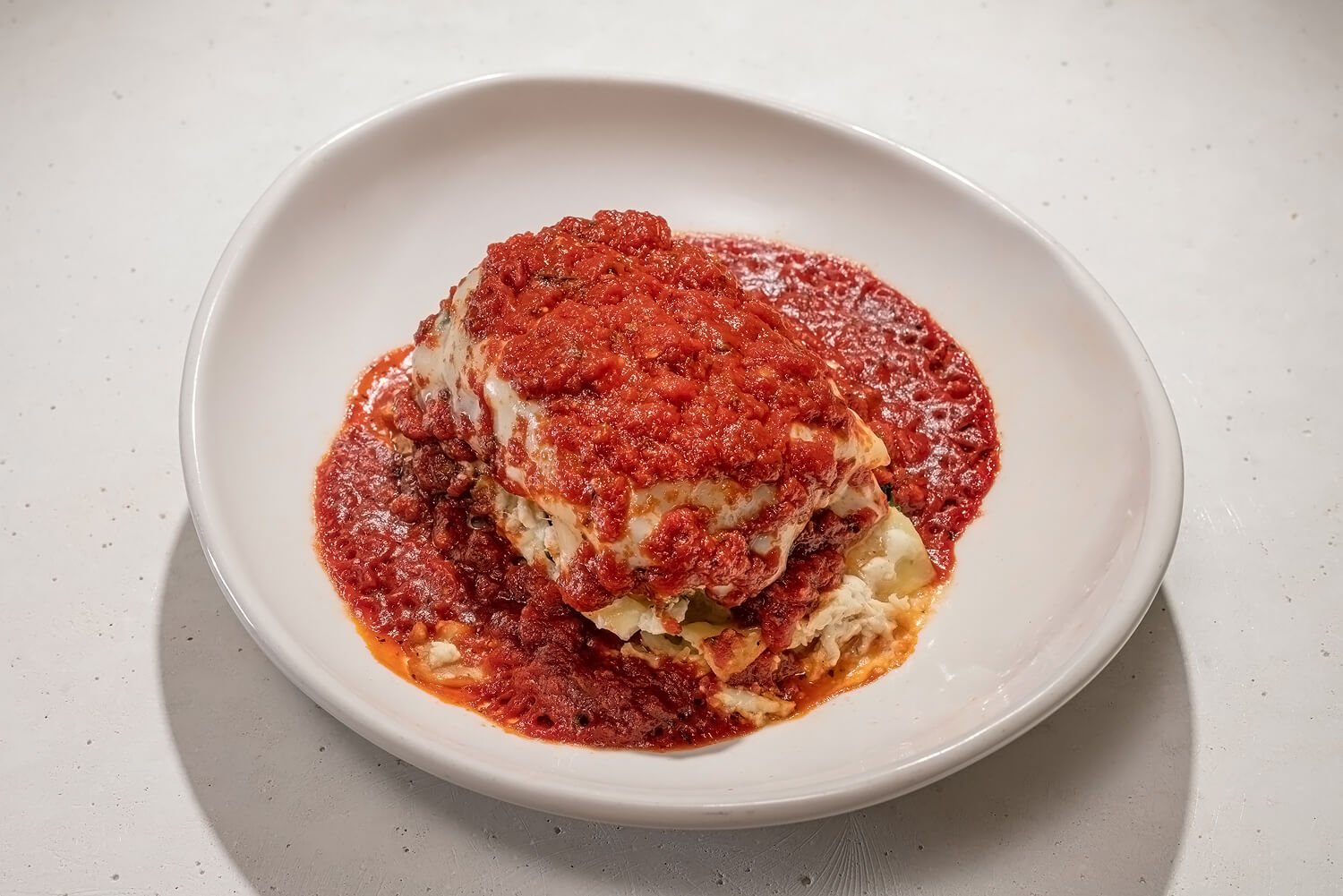 A serving of lasagna topped with marinara sauce, served on a white plate.