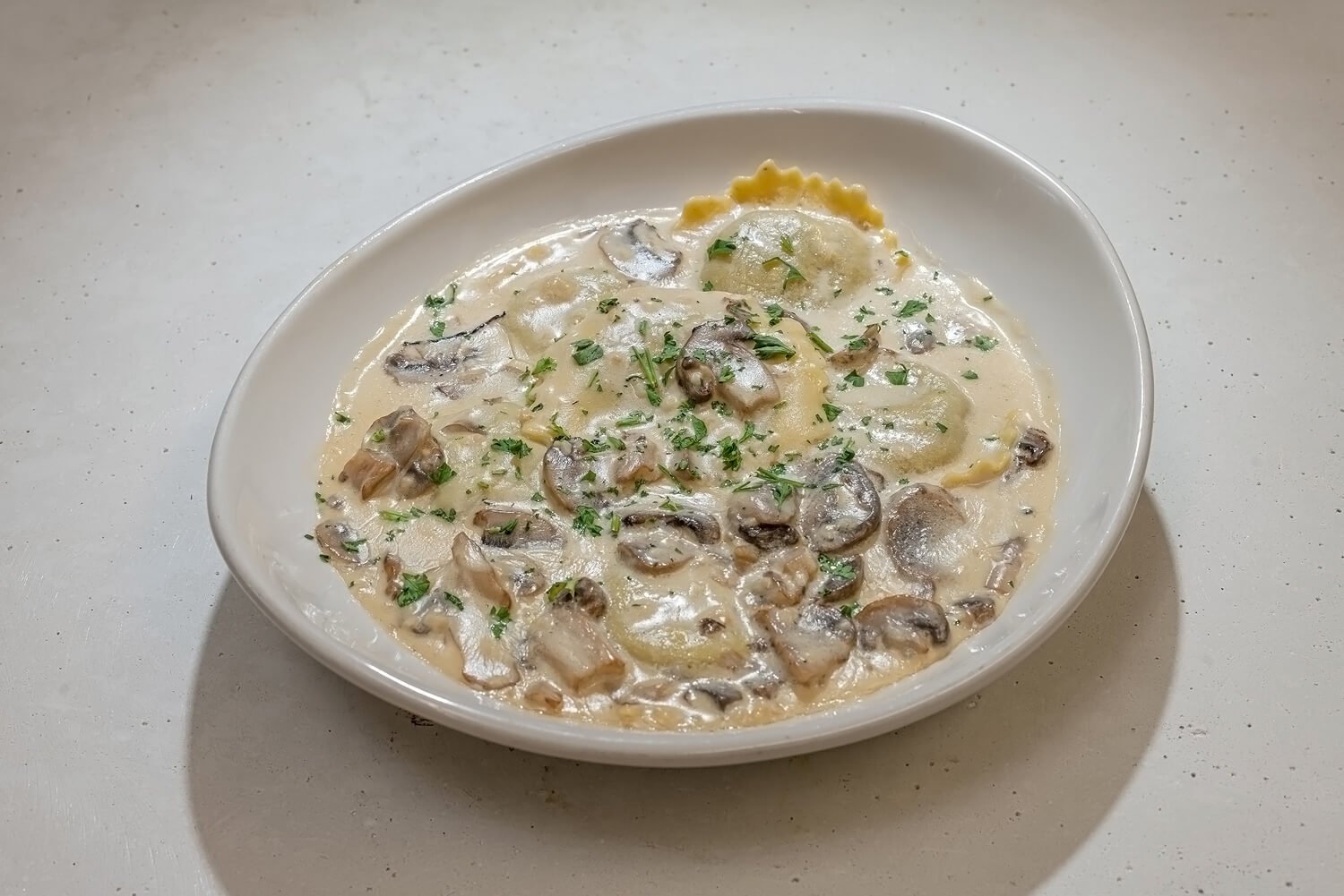 A plate of pasta with mushrooms in a creamy sauce, garnished with chopped parsley.